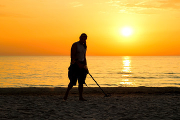 Man silhouette with metal detector on the beach