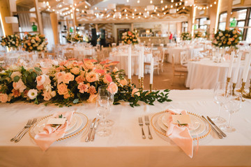 Coziness and style. Modern event design. Table setting at wedding reception. Floral compositions with beautiful flowers and greenery, candles, laying and plates on decorated table.