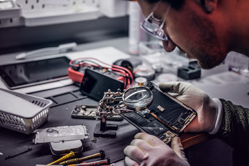 The technician uses a magnifying glass to carefully inspect the internal parts of the smartphone in...