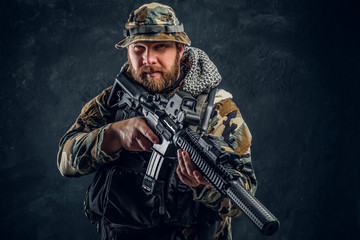 Brutal man in the military camouflaged uniform holding an assault rifle. Studio photo against a...