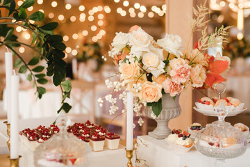 Candy bar with tasty desserts and appetizers at wedding reception. Decorated with flower compositions and candles. Sweet food, dessert, buffet, catering table, restaurant.