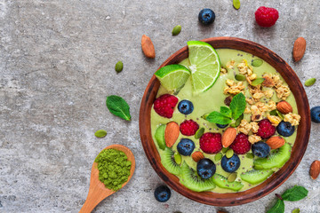 Obraz na płótnie Canvas matcha green tea smoothie bowl with fresh fruits, berries, nuts, seeds and granola for healthy vegetarian diet breakfast