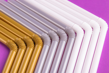 Colorful plastic drinking straws tightly pressed against each other on a purple table, close-up as background.