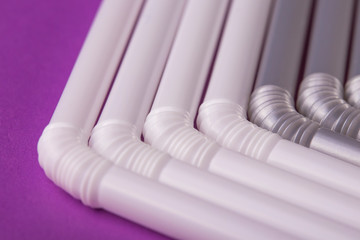 Colorful plastic drinking straws tightly pressed against each other on a purple table, close-up as background.
