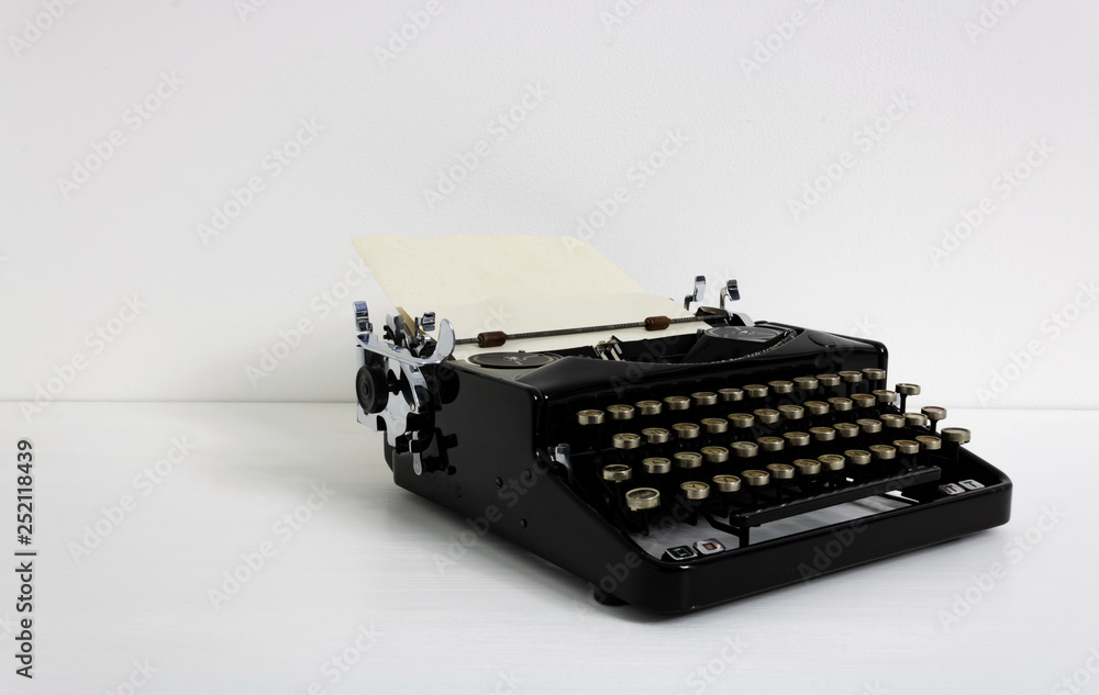 Fototapete old retro vintage black mechanical typewriter in laid on white desk in front of white wall with pape