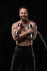 Obraz na płótnie Canvas Stylish bearded athletic young man posing with water splashes on face and chest while holding dumbbells