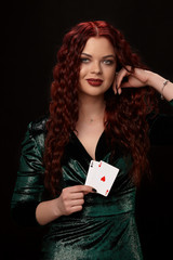 Sexy redheaded woman posing with a playing cards in her hands, on black background