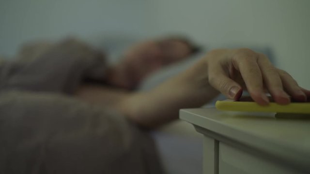 Rack focus of woman in reaching for snooze button on cell phone alarm / Murray, Utah, United States