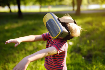 Little boy using virtual reality headset outdoor. VR, VR glasses, augmented reality experience.