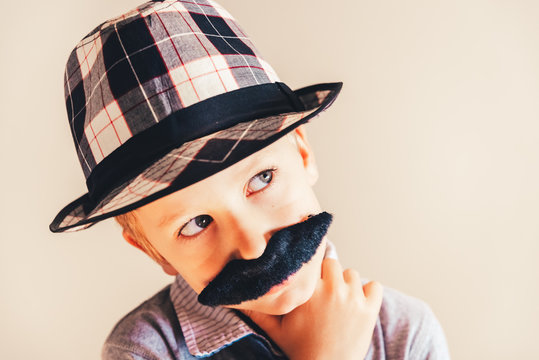 Funny portrait of pensive boy with fake mustache and hat, concept of childish humor, copy space.