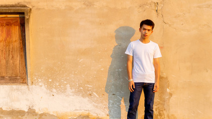 Plakat A young Thai boy is standing front of the dirty wall in the white shirt with moody face