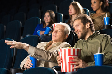 Senior man enjoying movies with his mature son together at the cinema
