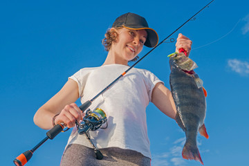 Happy fisher girl with perch fish trophy at the boat