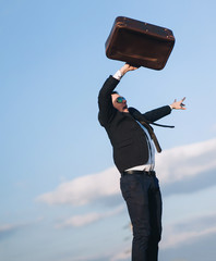 The young businessman threw up his hands with a suitcase and is trying to stay on his feet after...