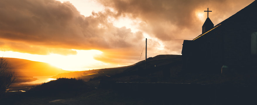 A lone abonded church hides away in the hills alongside a lake in the Peak District, UK during an amazing sunset