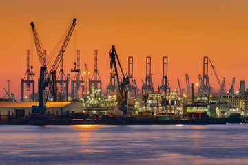 Obraz premium Cranes silhouetted against the evening sky in Hamburg Harbor, Germany, at dusk. The Port of Hamburg (Hamburger Hafen) is a sea port on the river Elbe. It is Germany's largest harbor.