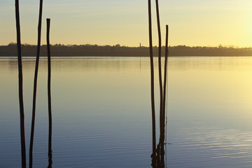 Reflect of sunset at the calm river, with wooden sticks on the first plan