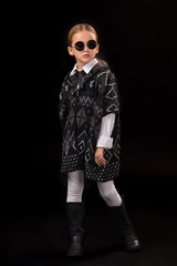 Little girl in a black glasses, dark poncho, black boots and a clutch in her hand
