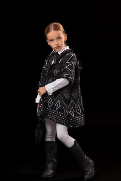 Little girl in a dark poncho, black boots and a clutch in her hand