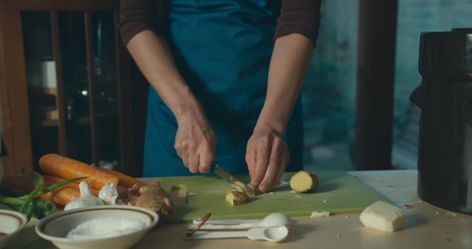 Young woman making fermented kimchi at home and cutting ginger