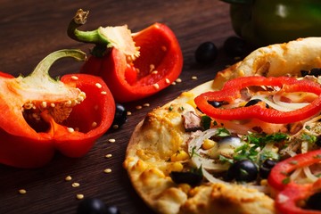 Vegetarian mushrooms Italian pizza with melted cheese, red pepper, corn, onion, black olives and fresh herb spices on a brown table decorated by mushrooms, black olives, red green pepper and arugula