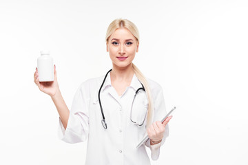 Attractive young female doctor with stethoscope pointing at white pill bottle isolated on white background