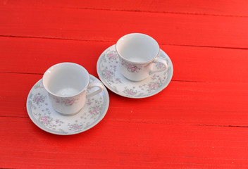 Empty white coffe cups with flower design on red wooden table. Two coffe cups