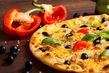 Close up vegetarian tuna Italian pizza melted cheese, black olives, red cherry tomatoes and fresh green basil leaves on a brown table decorated by mushrooms, black olives, red pepper and fresh arugula