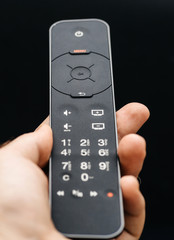 Man hand holding television remote control against black background 