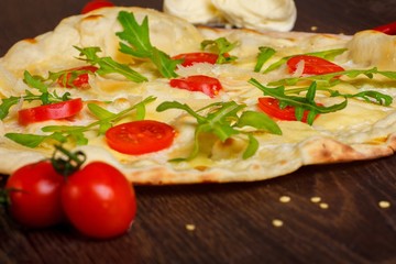Fototapeta na wymiar Vegetarian Italian pizza with melted mozzarella, parmezan cheese, red tomatoes and fresh green arugula leaves on a brown table decorated by mozzarella, red sweet pepper, cherry tomatoes and battledore