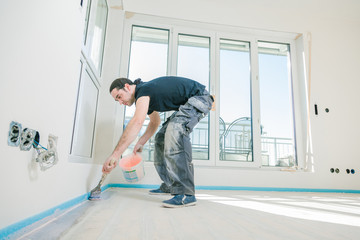 House under construction. Worker puts primer on concrete floor.