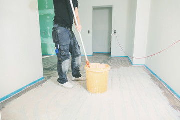 Fototapeta premium House under construction. Worker puts primer on concrete floor.