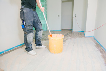 House under construction. Worker puts primer on concrete floor.