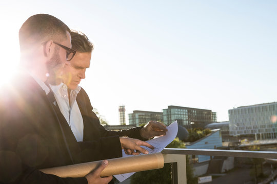 Two architects with blueprint discussing on a bridge in the city