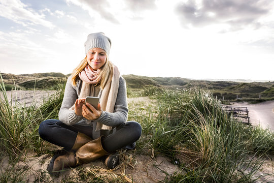 Smiling woman sitting in dunes using cell phones