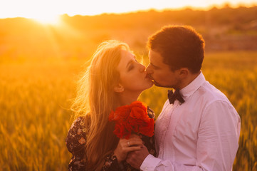 Man gives to woman bouquet of poppies in wheat field on the dusk