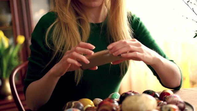 Beautiful woman taking photo with cellphone of easter egg plate, super slow motion