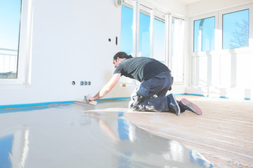 Plasterer during floor covering works with self-levelling cement mortar.