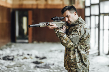 A military soldier targets and holds a large rifle in the building