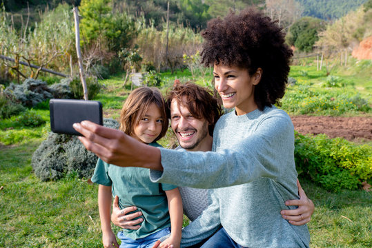 Happy family sitting on a bench in a garden, mother taking selfies