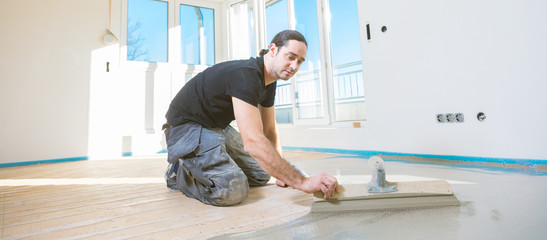 Plasterer during floor covering works with self-levelling cement mortar.