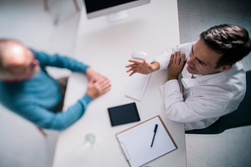 Top view of doctor talking to senior patient in medical practice