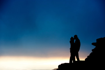 Silueta de pareja besándose en roca junto paisaje al atardecer