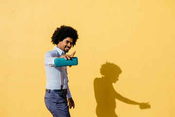 Smiling man with loudspeaker listening music and dancing in front of yellow wall