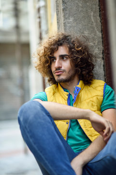 Portrait of young man with beard and curly hair wearing yellow waistcoat watching something