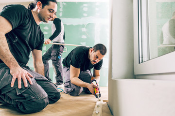 Mann mit der Kleberspritze befestigt die Sockelleiste an einer Baustelle. Parkettboden verlegen.