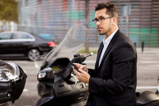 Businessman at motor scooter in the city using cell phone