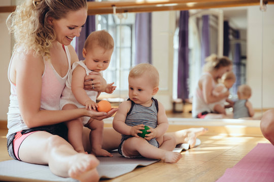 Mother with playing twin babies sitting on yoga mat
