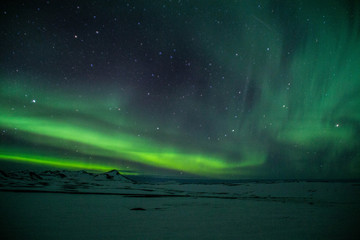 Winter scenic landscape night view of  Aurora Borealis/Northern lights dancing on the clear sky full of stars above snow covered mountains. Mývatn, North Iceland. Beautiful winter background scene. 