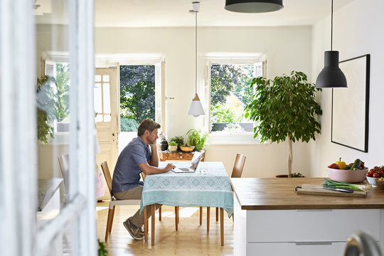 Mature man sitting in his dining room, using laptop